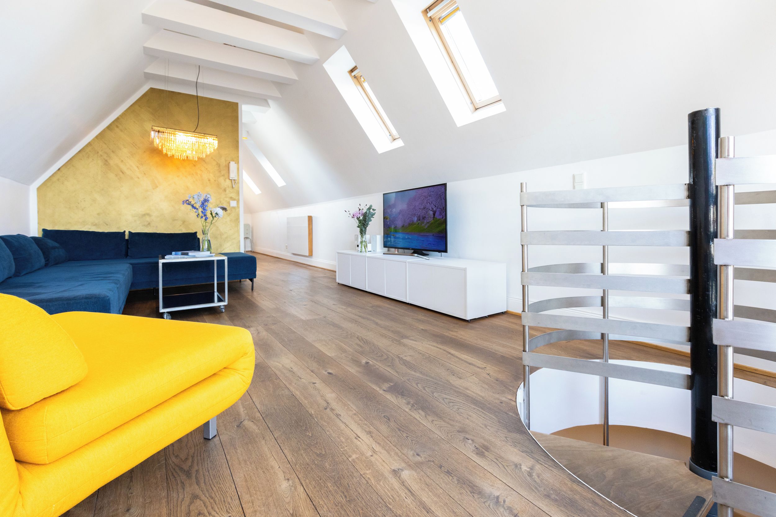A modern living room with a sectional sofa, a yellow armchair, a TV, and a white entertainment unit.