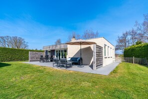 Una casa moderna con un patio, mobiliario exterior y una zona de barbacoa.