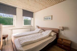 Ein Schlafzimmer mit einem Doppelbett, einem Nachttisch, einer Lampe und einem Fenster mit Blick auf Grünflächen.