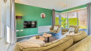 A modern living room with a green accent wall, a flat-screen TV, a sofa, a coffee table, and a chair. - Tastefully Furnished Detached Bungalow (De Koog)