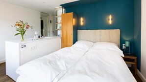 A hotel room with a bed, a wooden wardrobe, a white dresser, a mirror, and a wall-mounted light fixture. - Small studio apartment with a view over Cologne (Köln)