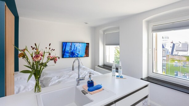 A modern bathroom with a white sink, a mirror, and a television mounted on the wall. - Small studio apartment with a view over Cologne (Köln)