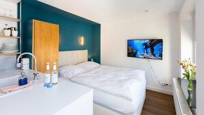 A hotel room with a bed, a TV mounted on the wall, a bathroom with a sink and toiletries, and a wooden wardrobe. - Small studio apartment with a view over Cologne (Köln)