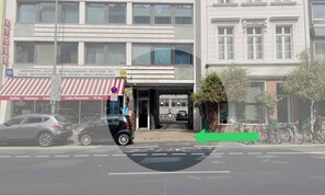 Straßenansicht eines Gebäudes mit einer Ladenfront, einem roten und weißen Streifenmarkisenvorzelt, einem Schild mit verschiedenen Firmennamen und einem Fahrradstellplatz.