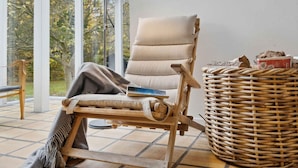 Een houten lounge stoel met kussen, een geweven mand en een lamp.