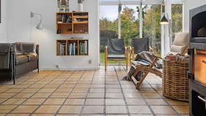 Een gezellige woonkamer met een open haard, een boekenkast, een bank en een groot raam met uitzicht op het omliggende landschap.