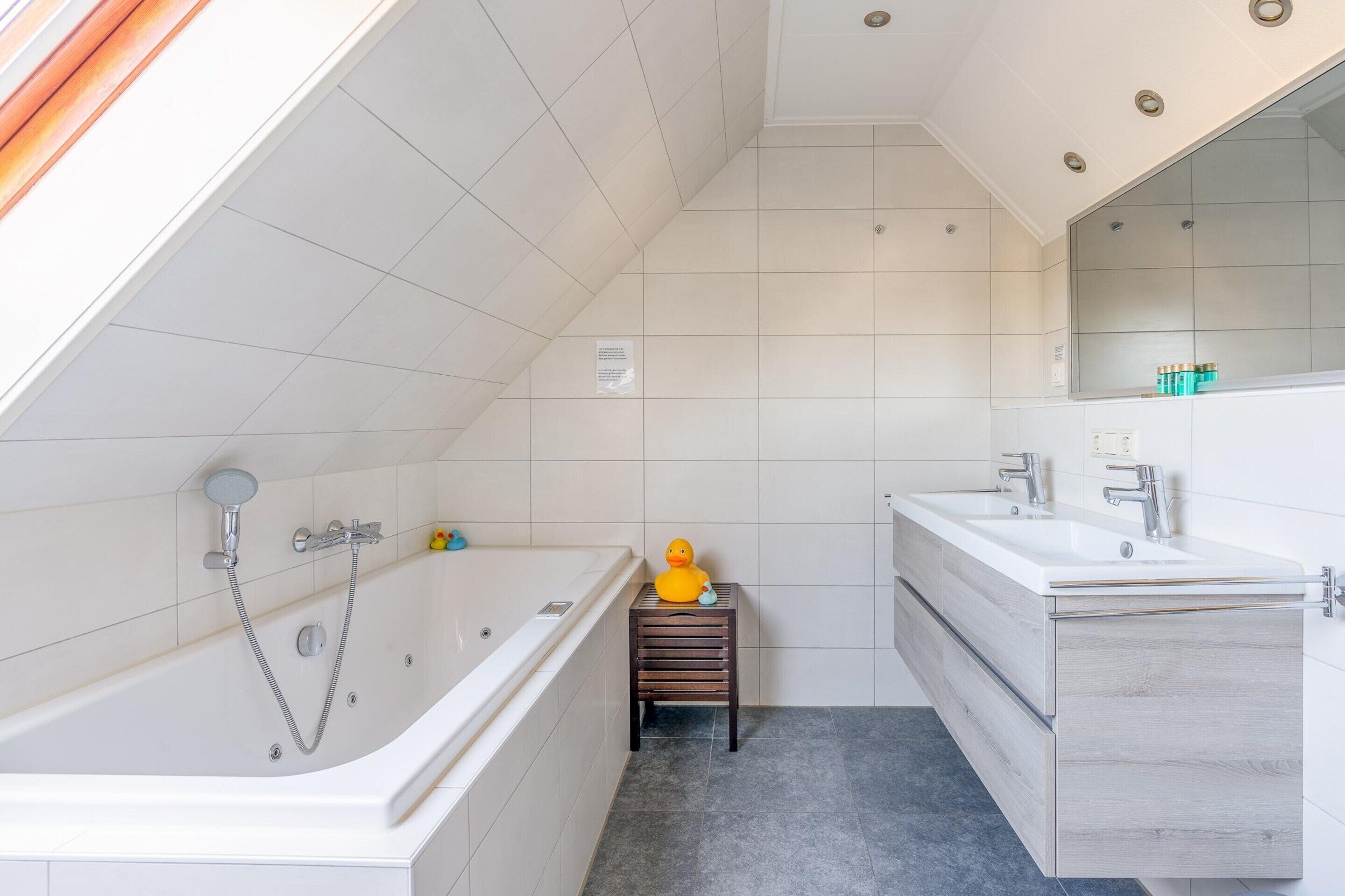 A modern bathroom with a bathtub, a small wooden stool, and a vanity with a mirror.