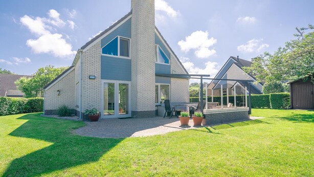 A two-story house with a large chimney, a covered patio, and a well-maintained lawn. - Charming Villa Near the sea and Forest (De Koog)