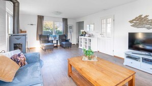 A spacious living room with a fireplace, a television, and a dining area. - Charming Villa Near the sea and Forest (De Koog)