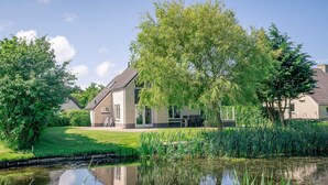 A residential property with a pond, a lawn, and a house with a sloped roof. - Charming Villa Near the sea and Forest (De Koog)