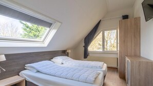 A bedroom with two beds, a skylight, a window, a wardrobe, and a bedside table. - Charming Villa Near the sea and Forest (De Koog)
