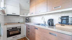 A modern kitchen with white cabinetry, a built-in oven, a coffee maker, and a kettle. - Charming Villa Near the sea and Forest (De Koog)