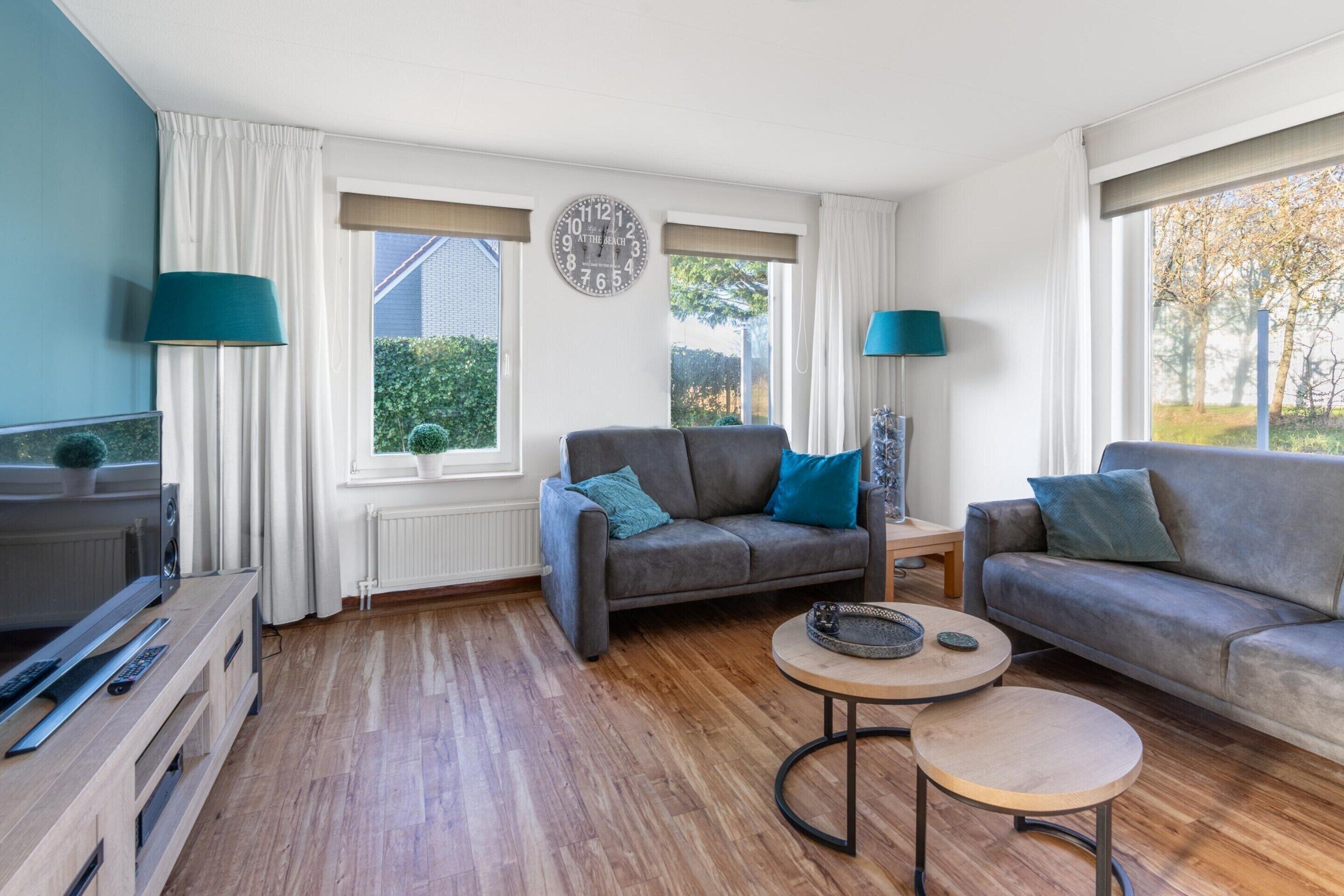 Ein modernes Wohnzimmer mit zwei Sofas, einem Couchtisch, einem Fernseher und einem großen Fenster mit Vorhängen.