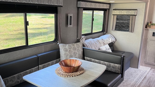 Interior acogedor de una caravana con mesa de comedor, asientos acolchados y ventanas amplias que ofrecen vistas al exterior.