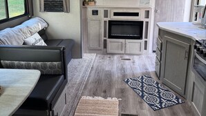 Interior compacto de una caravana, con zona de estar, kitchenette y televisor montado.