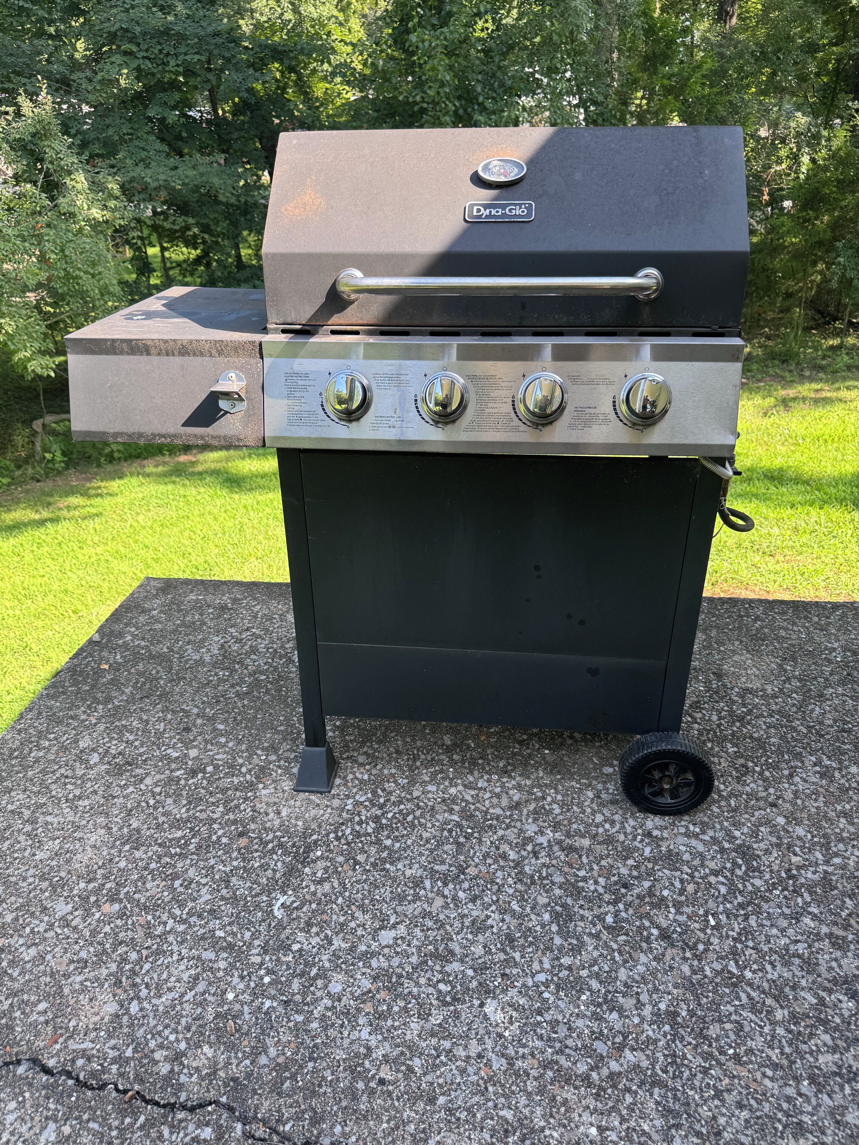 A black outdoor grill with four control knobs and a side drawer, placed on a concrete surface.