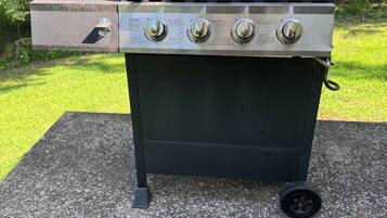 A black outdoor grill with four control knobs and a side drawer, placed on a concrete surface.