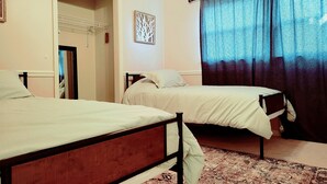Camera da letto con due letti singoli, un tappeto decorato, una porta che dà su un'altra stanza e una finestra con tende.