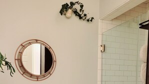 Un bagno con il water, uno specchio rotondo e un box doccia in vetro.
