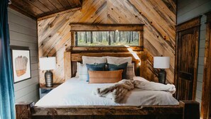A cozy bedroom with a large bed, wooden headboard, and a window overlooking a forest. - Movie under Stars, Heated Pool, Pickle ball, Slide (Broken Bow)
