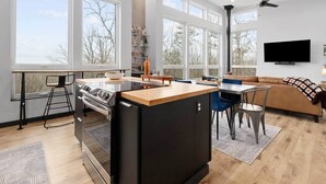 Une cuisine moderne dotée d’un îlot central, d’un coin repas avec des chaises, d’un canapé et d’un téléviseur fixé au mur.