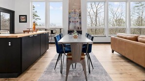 Une cuisine moderne avec un coin repas, de grandes fenêtres et une vue sur les arbres.