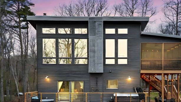 Une maison moderne à deux étages, dotée de grandes fenêtres, d’une terrasse et d’un escalier.