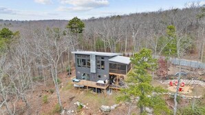 A modern two-story house with a deck, surrounded by a forested area. - Treetop Cabin. Private & modern w/ hot tub & view (Dunlap)