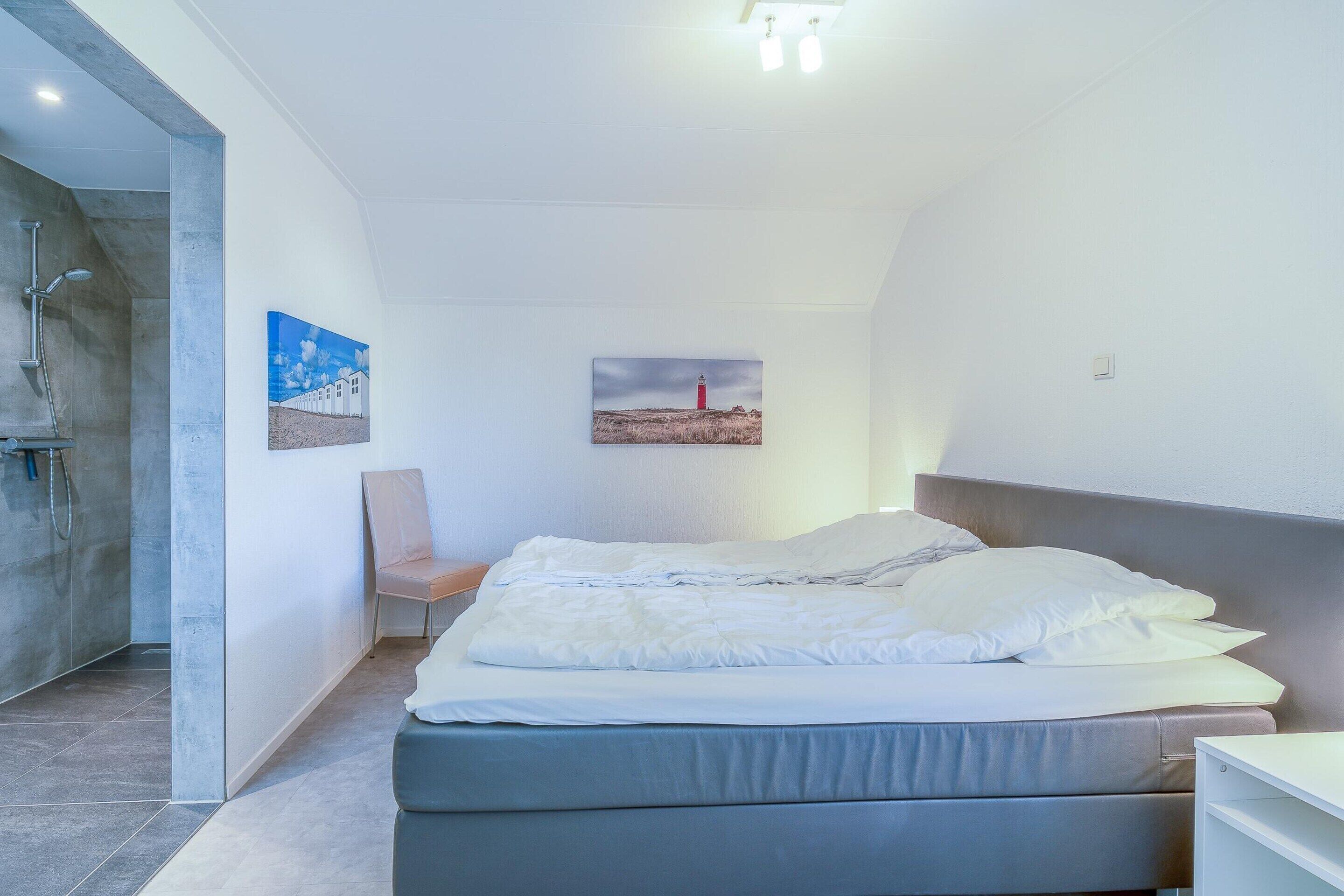 A modern bedroom with a bed, a chair, and two paintings on the wall.