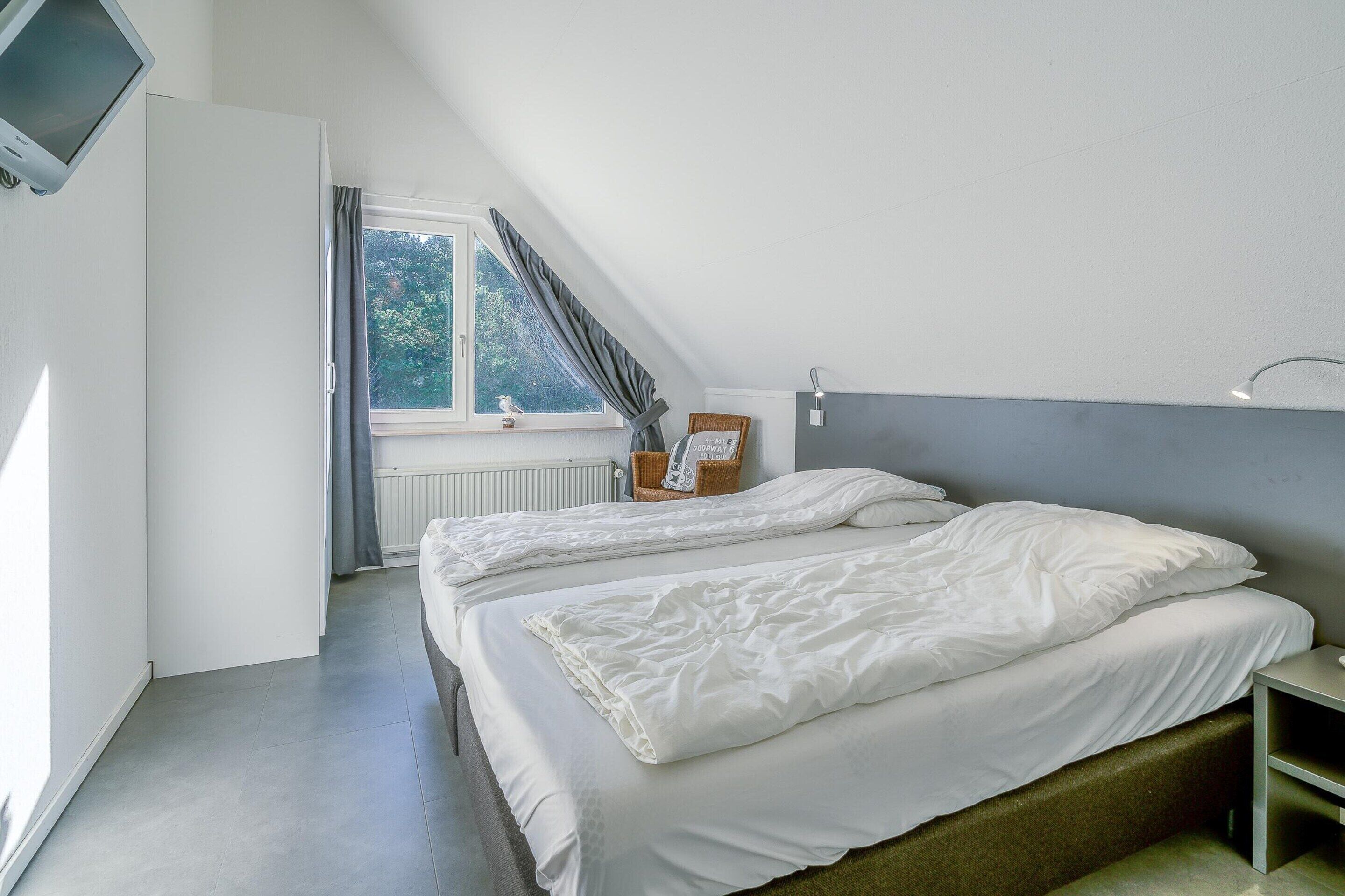 A bedroom with two beds, a window with curtains, a radiator, and a television mounted on the wall.