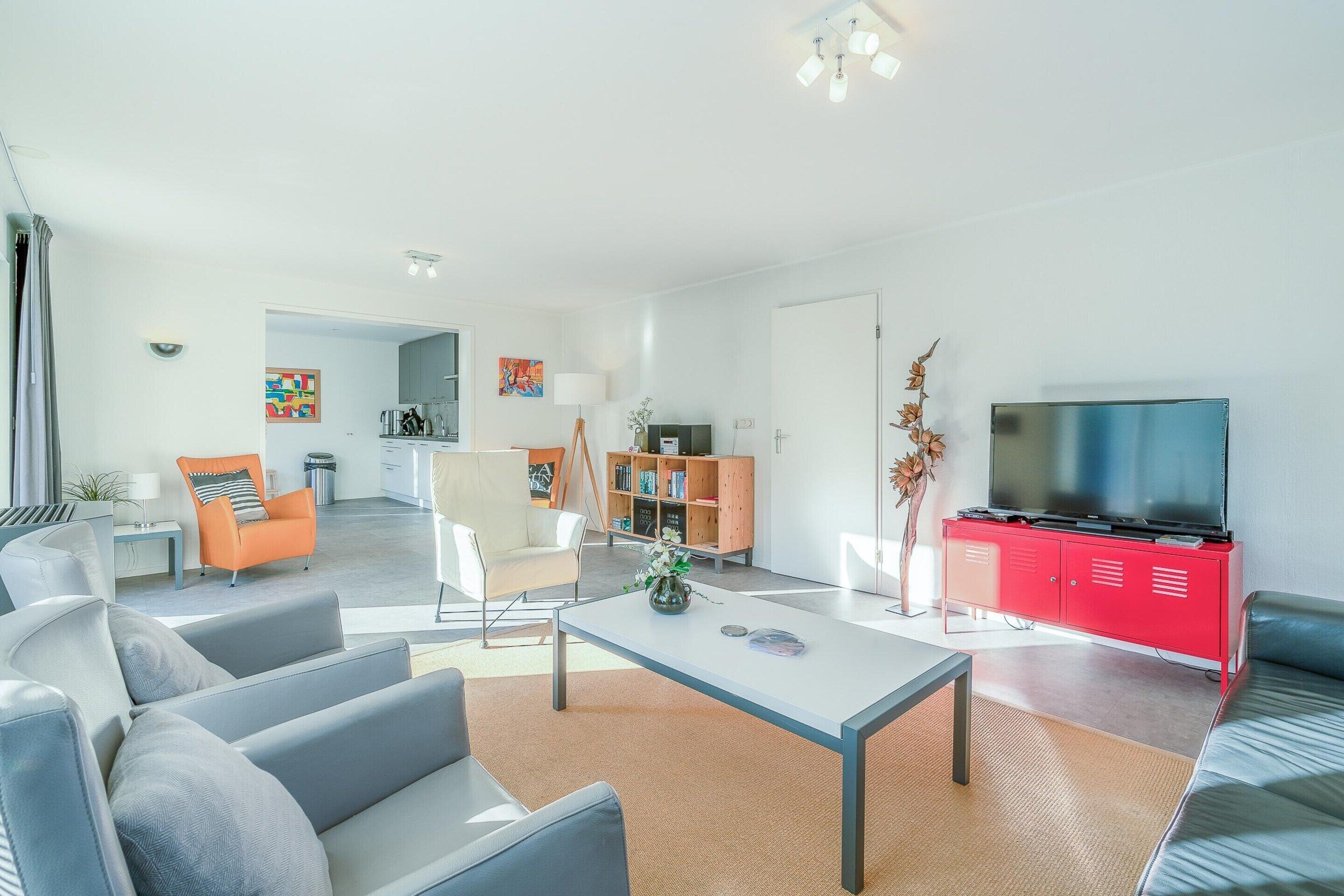 A modern living room with a grey sofa, a coffee table, and a red entertainment unit with a TV.