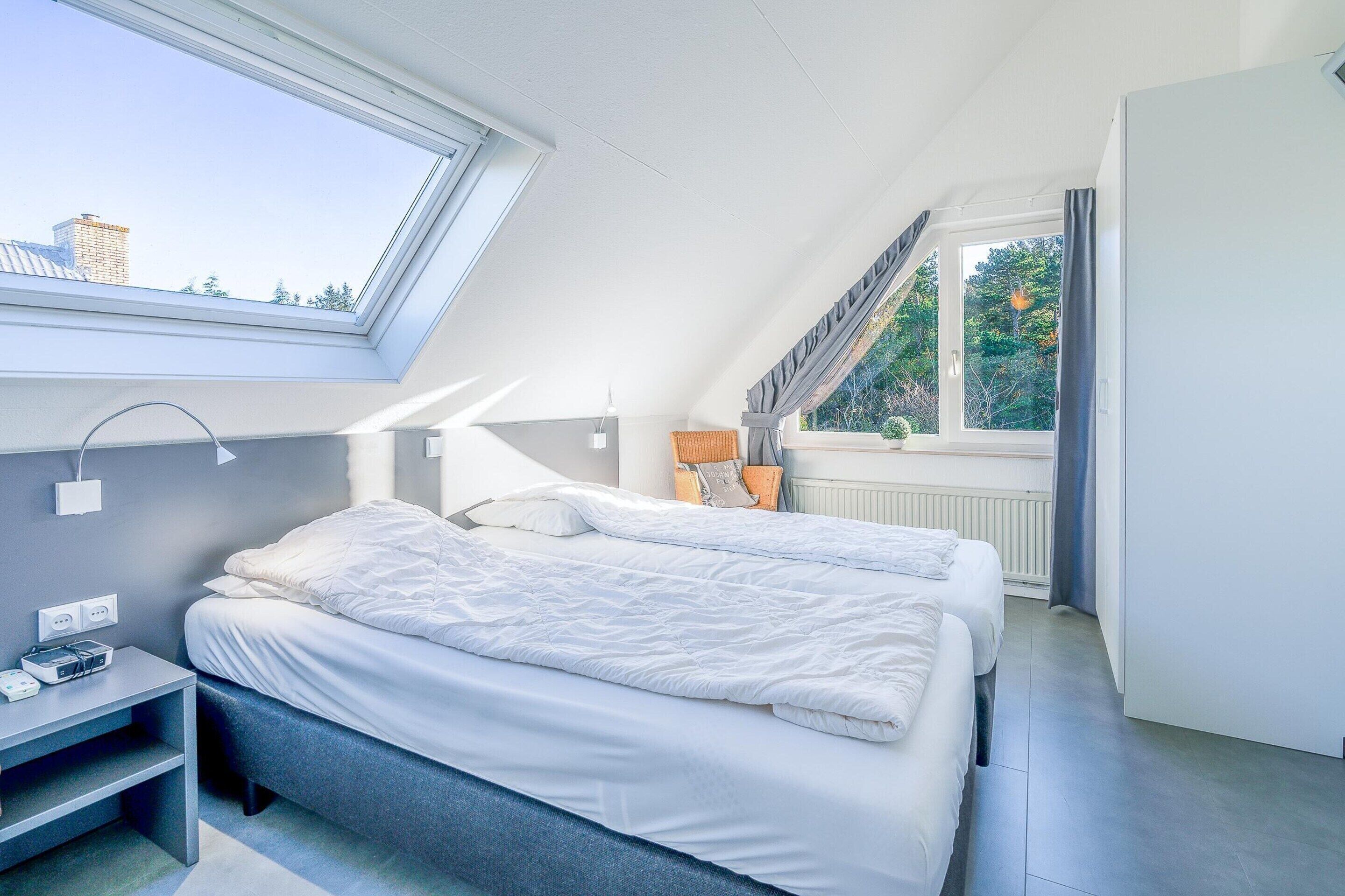 Camera da letto moderna con lucernario, due letti, un comodino con lampada e vista sull'esterno.