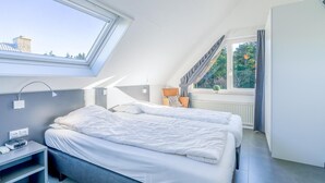 Een moderne slaapkamer met dakraam, twee bedden, een nachtkastje met lamp en uitzicht op de omgeving.