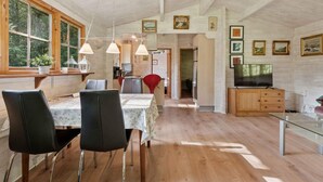 Un grand espace à manger avec une table et des chaises en bois, une cuisine à l’arrière-plan et un téléviseur posé sur un meuble en bois.