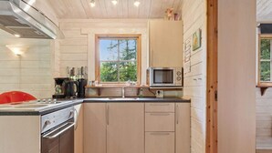 Une cuisine compacte avec des meubles en bois, un four à micro-ondes, une cuisinière et une fenêtre donnant sur un paysage verdoyant.