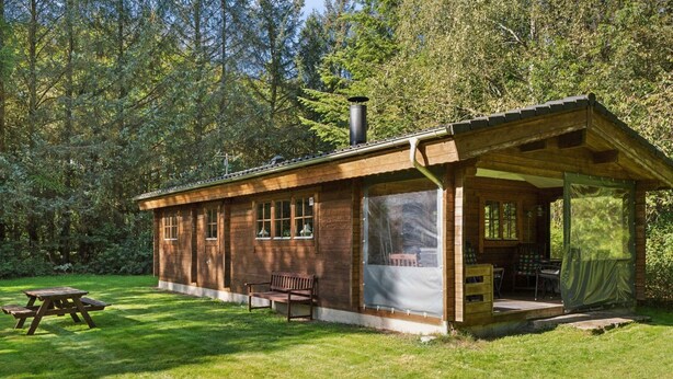 Une cabane en bois dotée d’un porche couvert, d’une table de pique-nique et d’un banc.