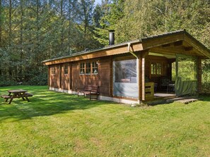 En træhytte med en overdækket veranda, et picnicbord og en bænk.