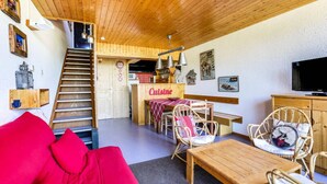 A cozy living area with a wooden staircase, a red sofa, wicker chairs, a wooden table, and a kitchenette labeled 'Cuisine'. - Pleasant 2-room Apartment for 7 People in Arc 1600 in a Residence With Outdoor Swimming Pool Close to the Slopes and Shops (Bourg-Saint-Maurice)