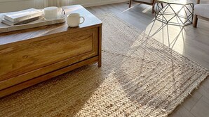 Uma sala de estar moderna com uma janela grande, uma mesa de centro de madeira, um sofá e um tapete.