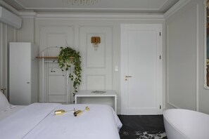 A hotel room with a bed, a bedside table, a hanging plant, a door, and a white wall.
