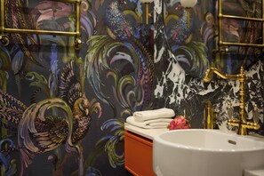 A bathroom with a peacock mural, a white sink, and a gold faucet.