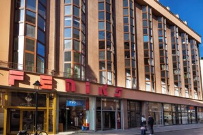 Un edificio de varios pisos con un llamativo letrero de 'FEDINE', locales comerciales y una bicicleta estacionada afuera.