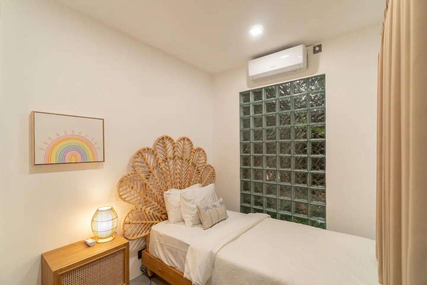 Een slaapkamer met een bed, een nachtkastje met een lamp, een wandairconditioner en een raam met uitzicht op bomen.