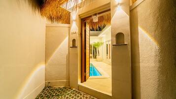 Un pasillo estrecho con una piscina visible a través de una puerta abierta, que conduce a una habitación luminosa.