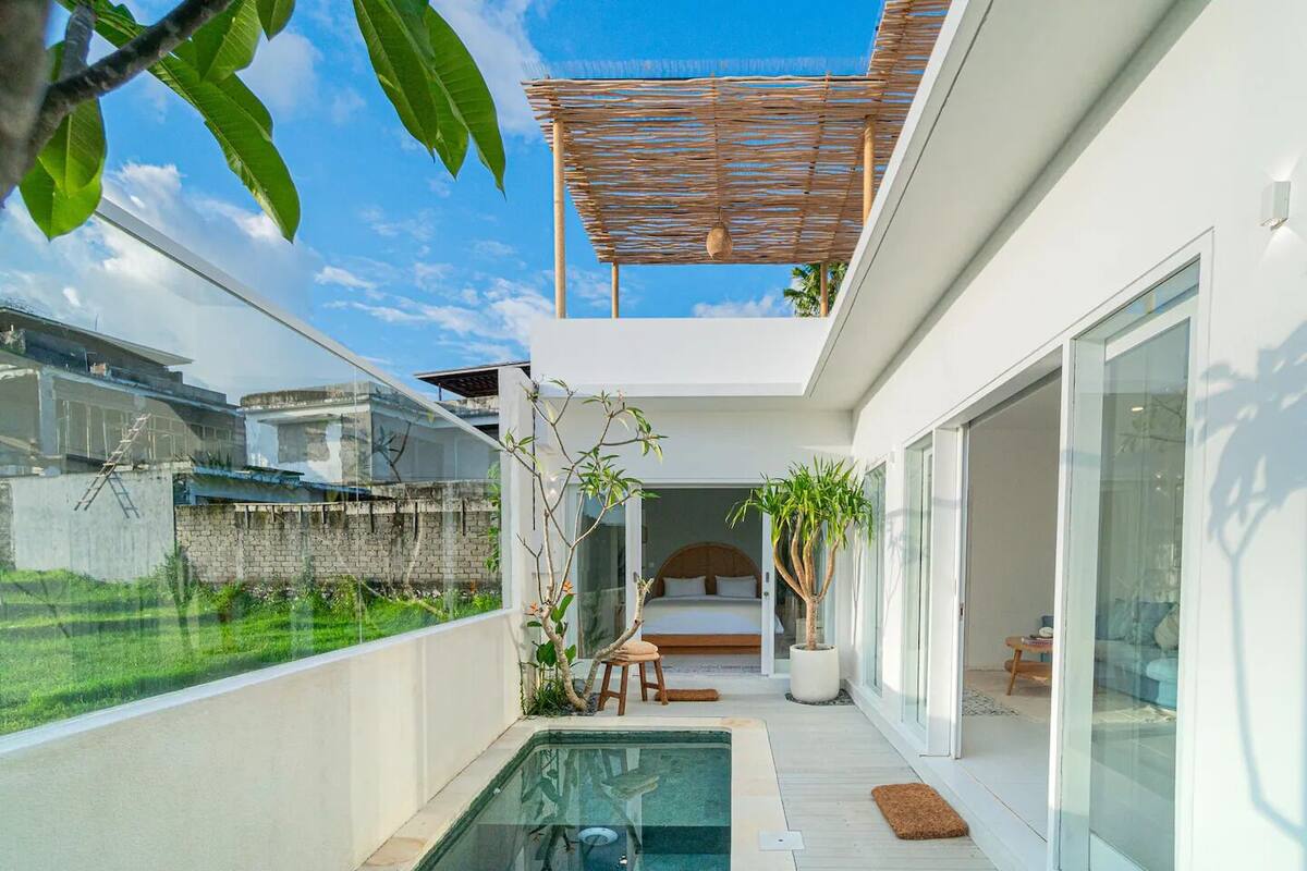 Ein moderner, offener Wohnbereich mit einem gläsernen Pool, einer Holzpergola und Blick auf die umliegende Grünfläche.