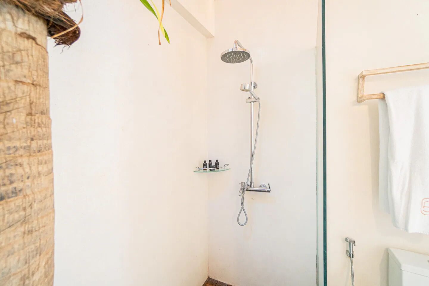 En bruser med håndbruser og vandhane på væggen. Der er en glashylde med toiletartikler.