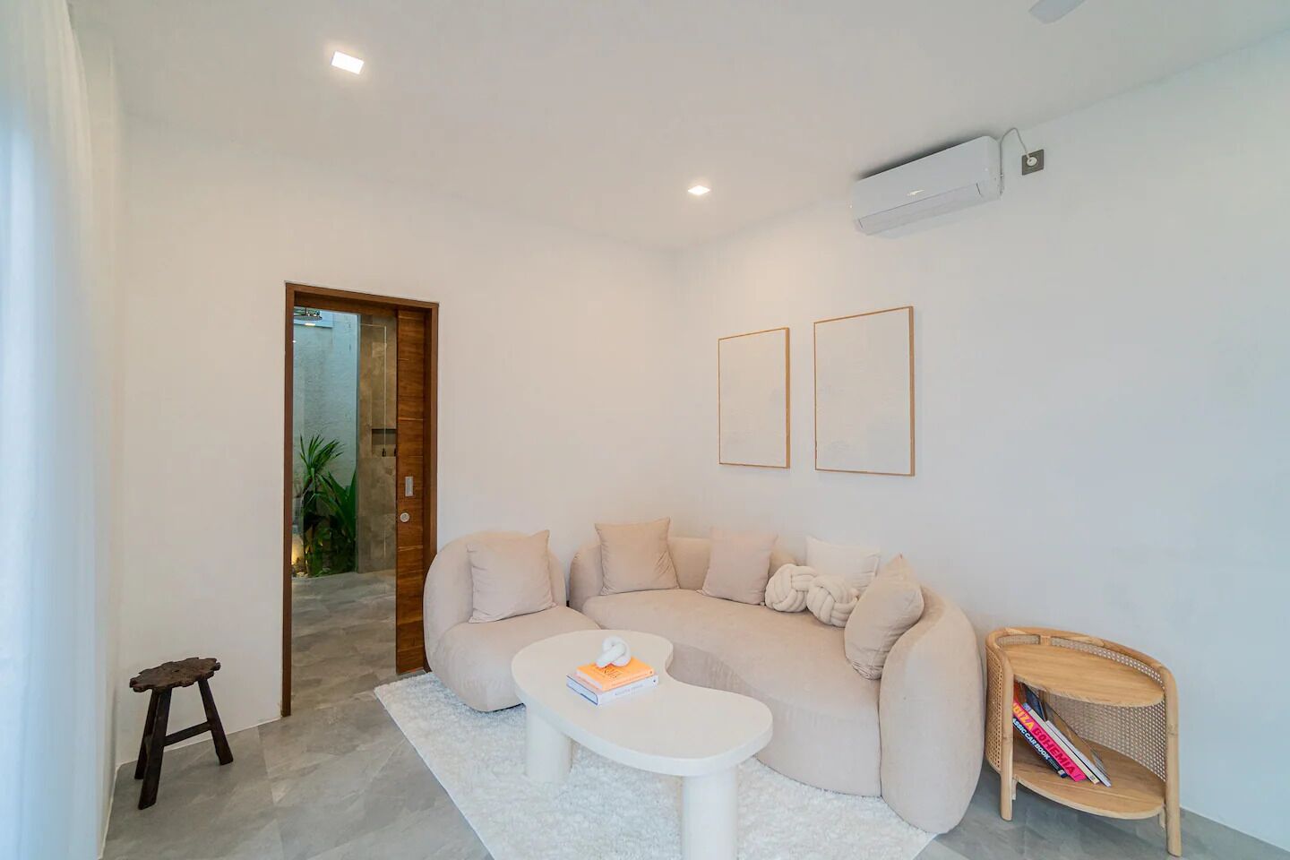 A modern living room with a beige sofa, a white coffee table, and a small wooden side table with magazines.