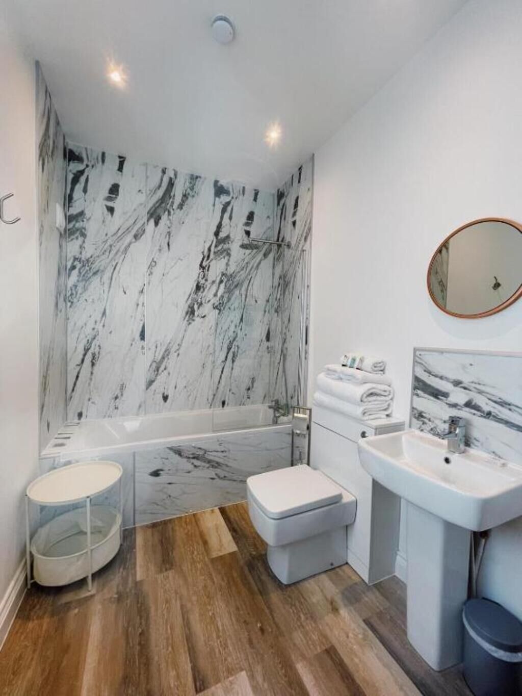 A modern bathroom with a marble wall, a bathtub, a toilet, a sink, and a mirror.