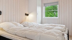 A bedroom with a bed, a wardrobe, and a window with a view of greenery. - 4 Star Holiday Home in Nexo (Nexø)
