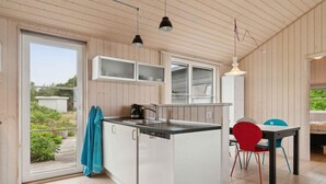 A modern kitchen with white cabinetry, a central island, and a dining area with mismatched chairs. - 4 Star Holiday Home in Nexo (Nexø)